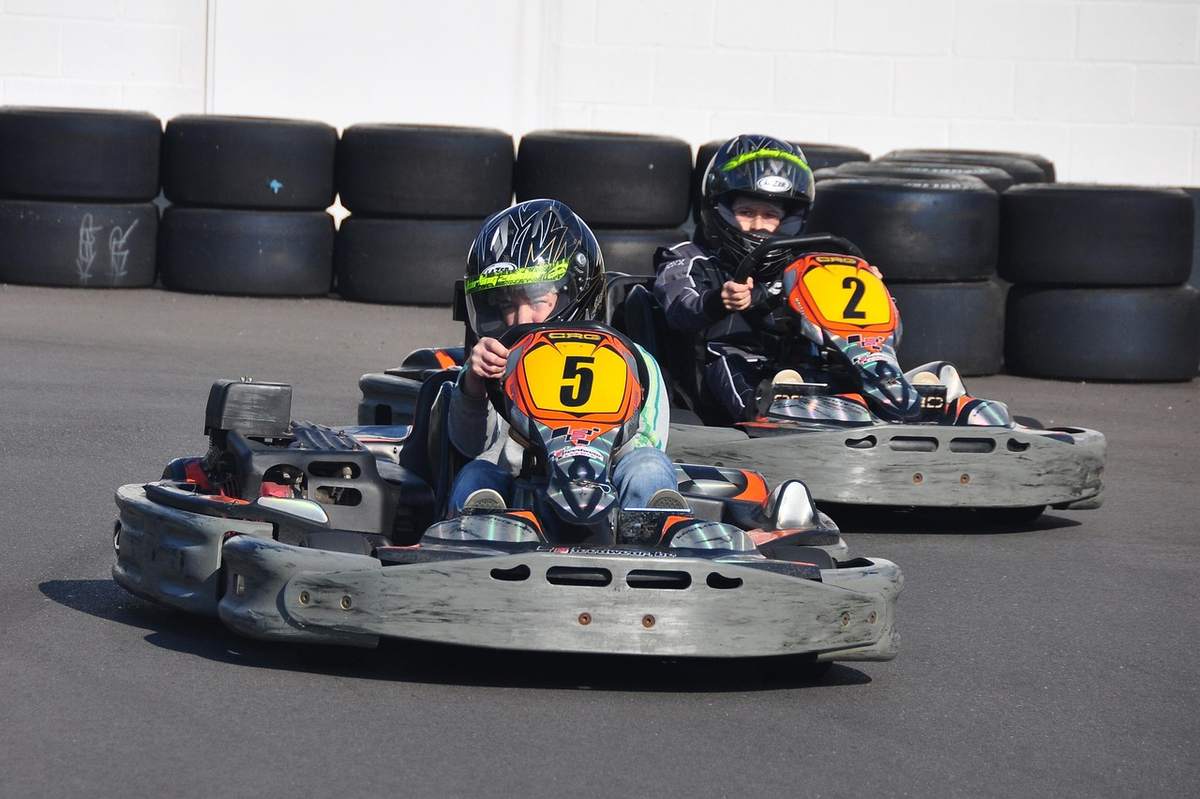 Trois jeunes pilotes en karts numérotés 5, 2 et 1 roulent sur une piste intérieure avec pneus de sécurité