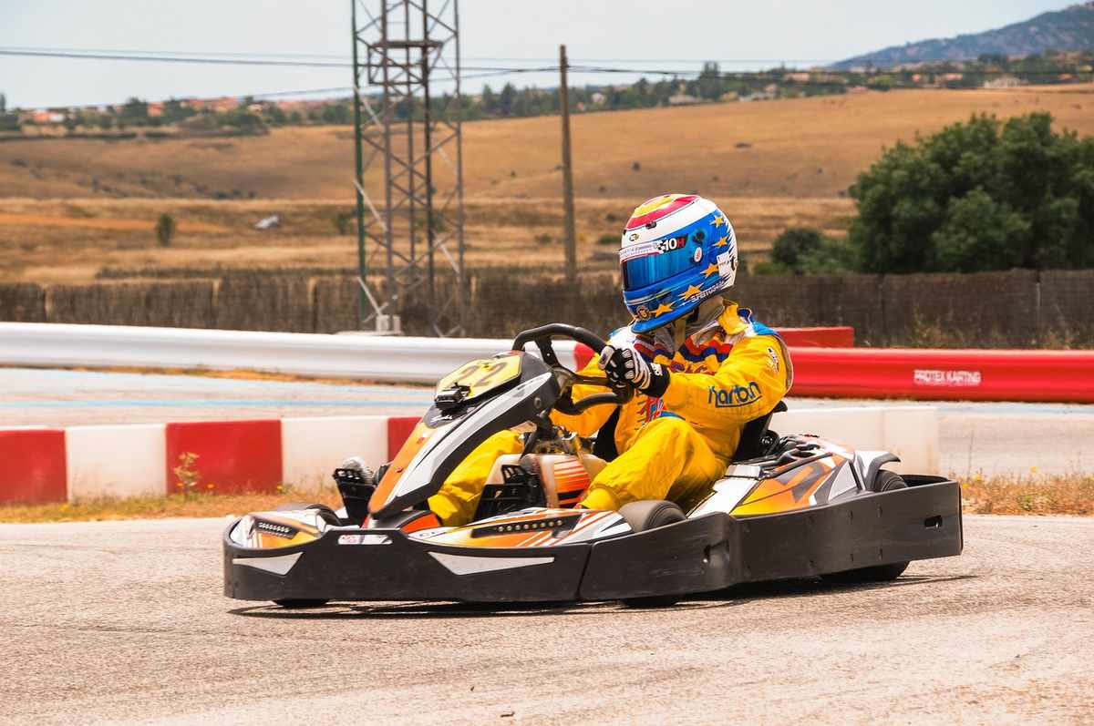 Pilote vêtu d'une combinaison jaune conduisant un kart sur une piste avec barrières rouges et blanches