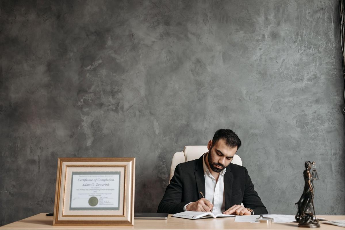 Un homme en costume écrit à un bureau avec un cadre et une statue devant lui Un homme en costume écrit à un bureau avec un cadre et une statue devant lui