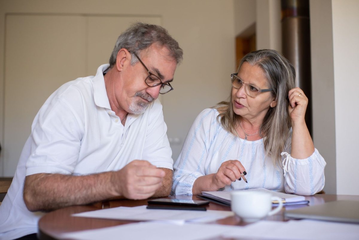 Homme et femme âgés en conversation, documents et tasse sur une table devant eux