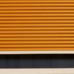 Volet roulant orange partiellement déroulé au-dessus d'une fenêtre sombre