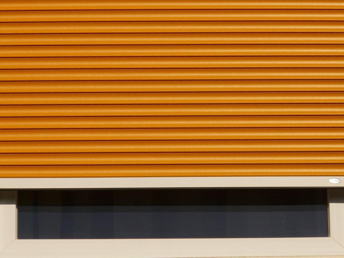 Volet roulant orange partiellement déroulé au-dessus d'une fenêtre sombre