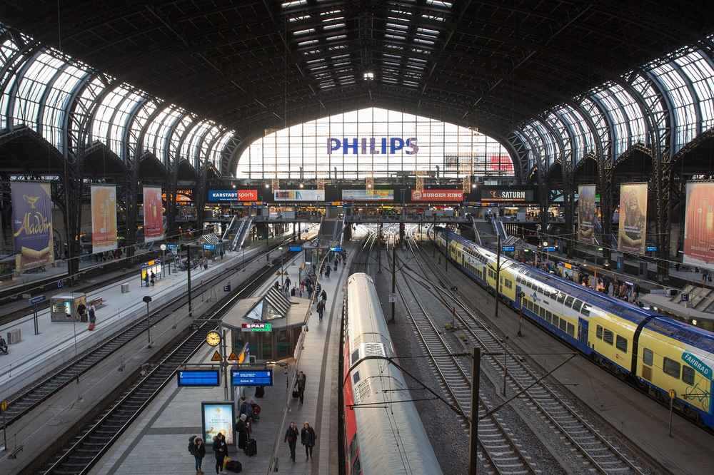 Intérieur d'une gare avec trains, voies et voyageurs sous une grande arche