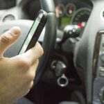 Une main tient un smartphone à l'intérieur d'une voiture, près du tableau de bord