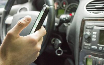 Une main tient un smartphone à l'intérieur d'une voiture, près du tableau de bord