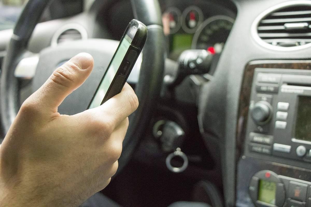 Une main tient un smartphone à l'intérieur d'une voiture, près du tableau de bord